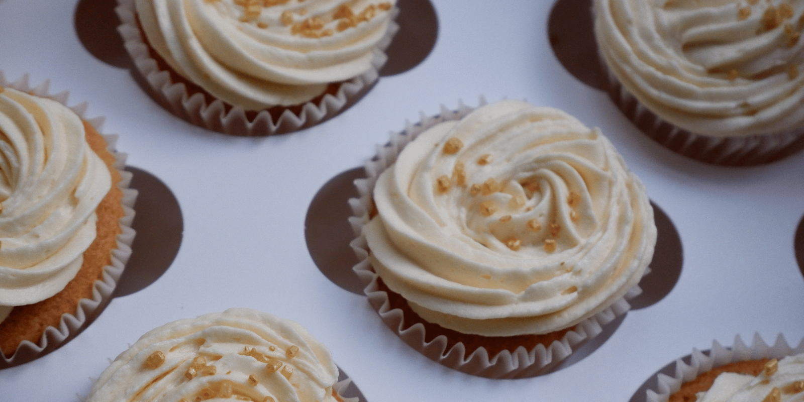 close up of multiple cupcake with vanilla buttercream and some gold sprinkles.